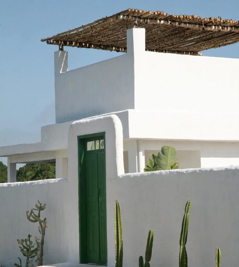 Fachada branca da Casa ILHAMAR com porta verde, pérgola de madeira e cactos